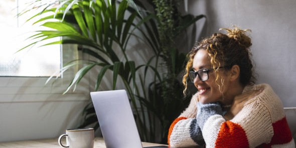 One adult woman watching laptop monitor smiling and enjoying online contents like movie or channels. Happy female people using computer at home alone and have fun. Modern lady sitting at the table